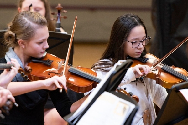 Students playing violin for orchestra concert.